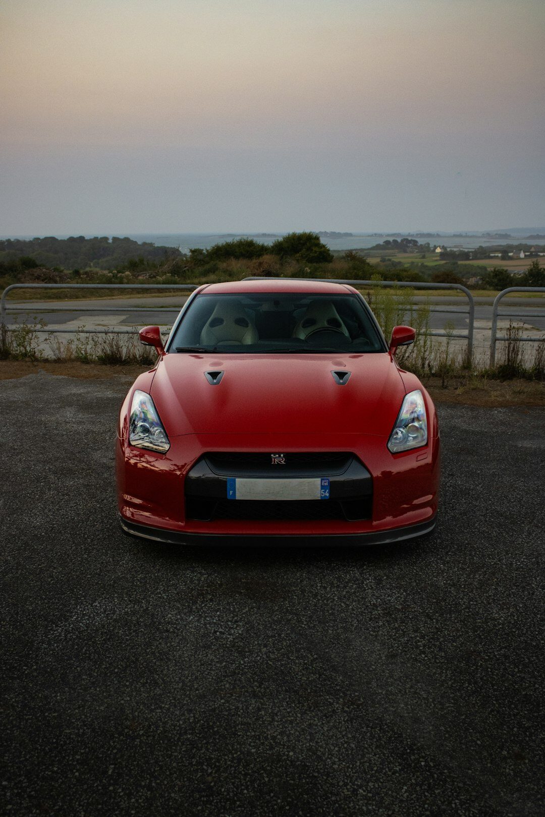 Red luxury sports car driving on an open coastal road at dusk
